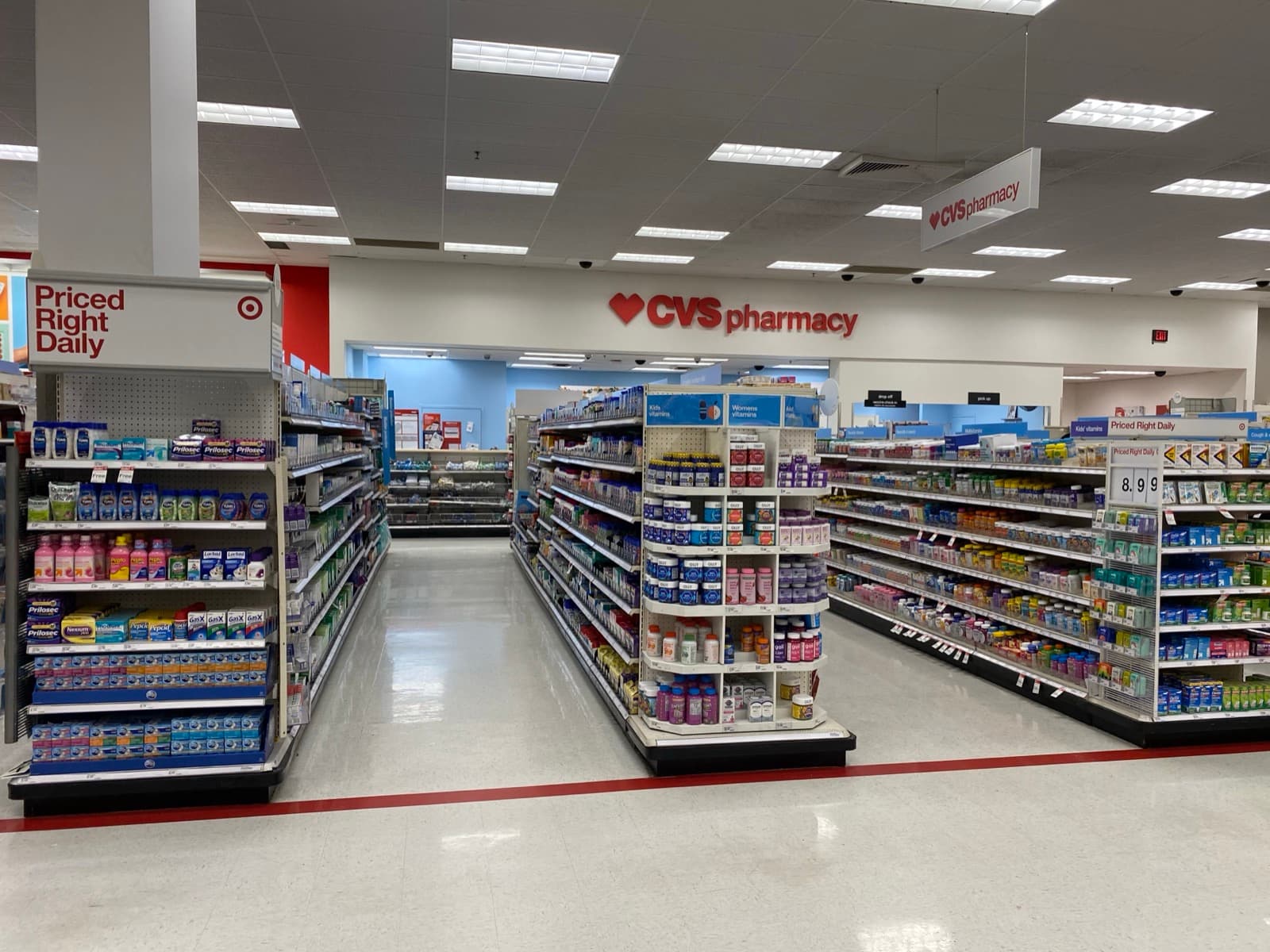 Aisles of over-the-counter medicines and vitamins leading toward a retail pharmacy counter.