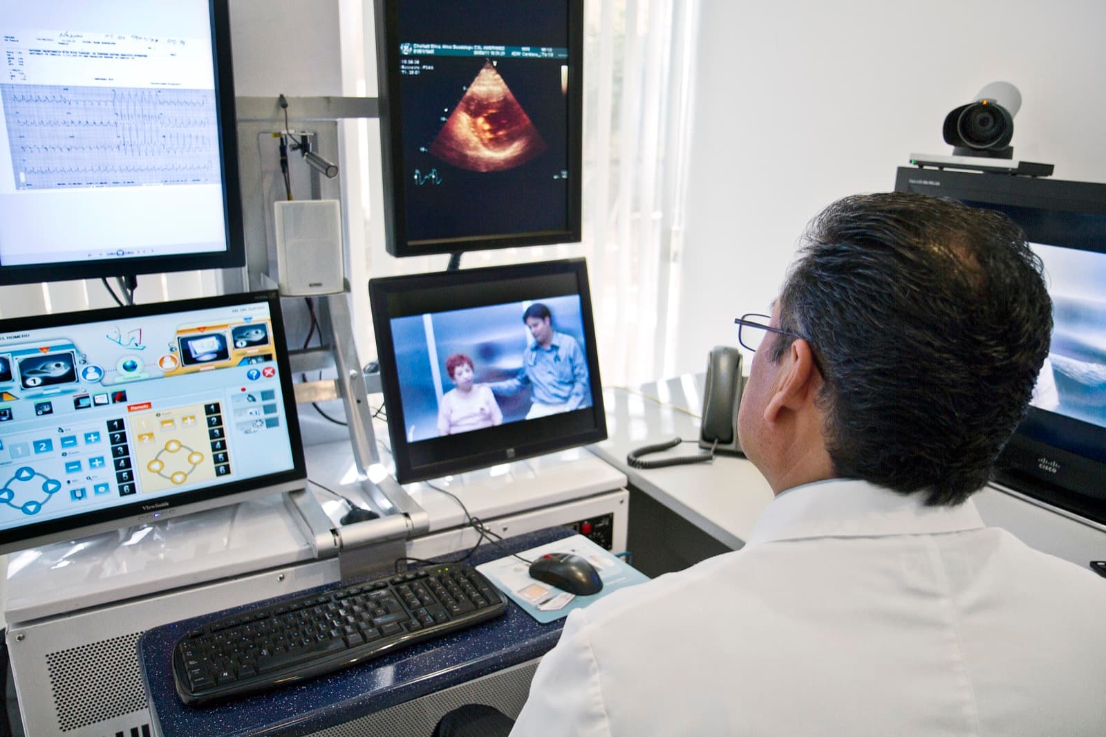 A physician monitors patient data and a live video consultation at a hospital telemedicine workstation.