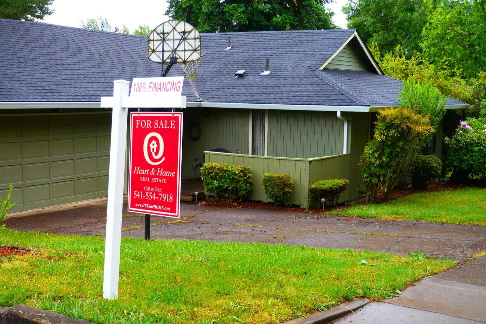 A red for-sale sign standing in front of a single-family house