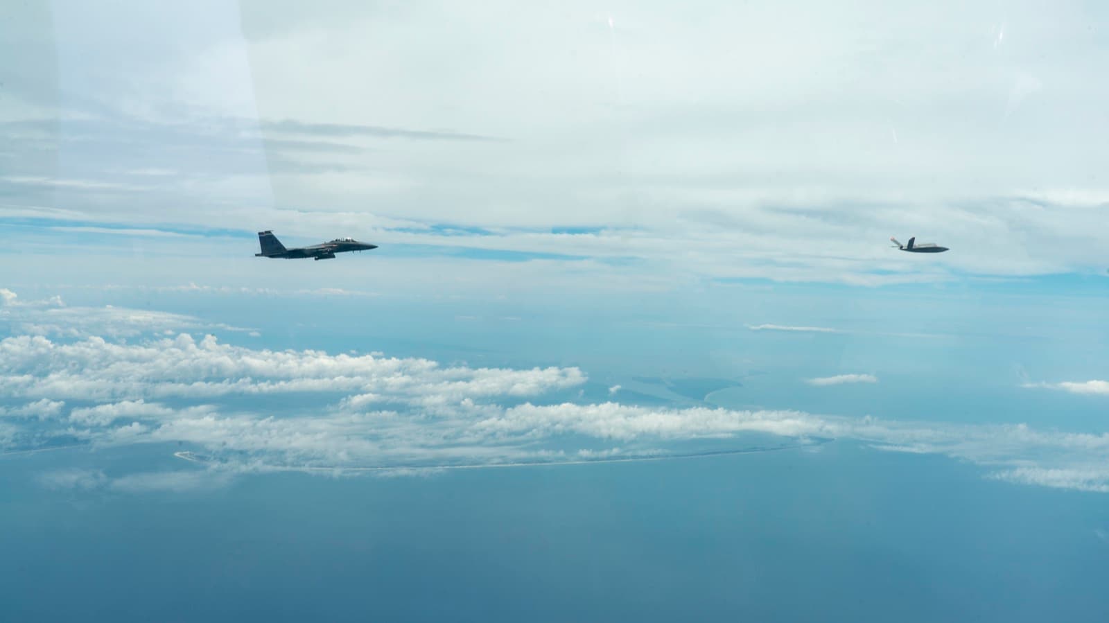 An XQ-58A Valkyrie autonomous jet flying in formation with a crewed F-15 fighter during a test flight.