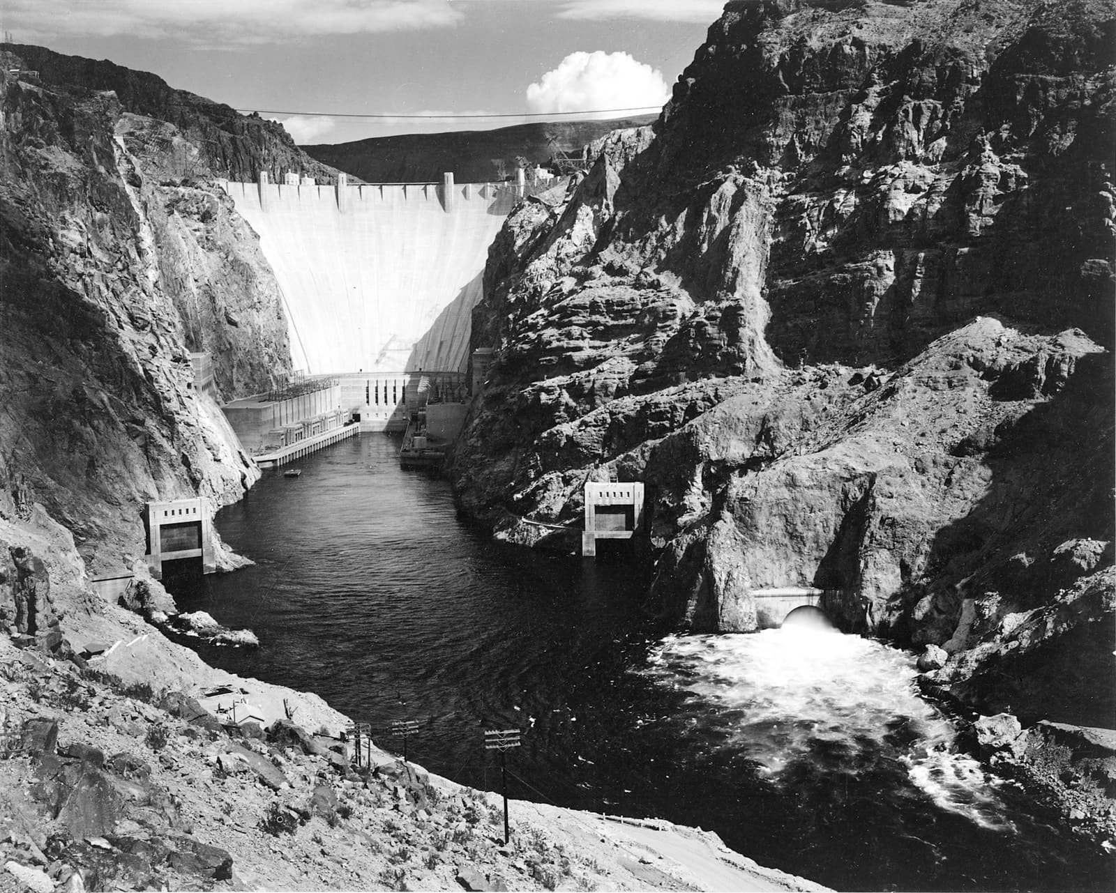 Ansel Adams's 1941 photograph of Boulder Dam rising above the Colorado River, power infrastructure threading the canyon below.