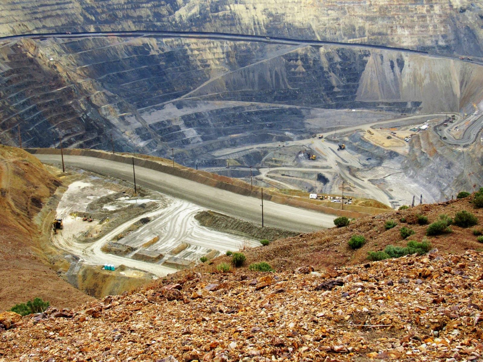 Terraced benches of the Bingham Canyon open-pit copper mine descending into the earth, haul roads and trucks visible far below.